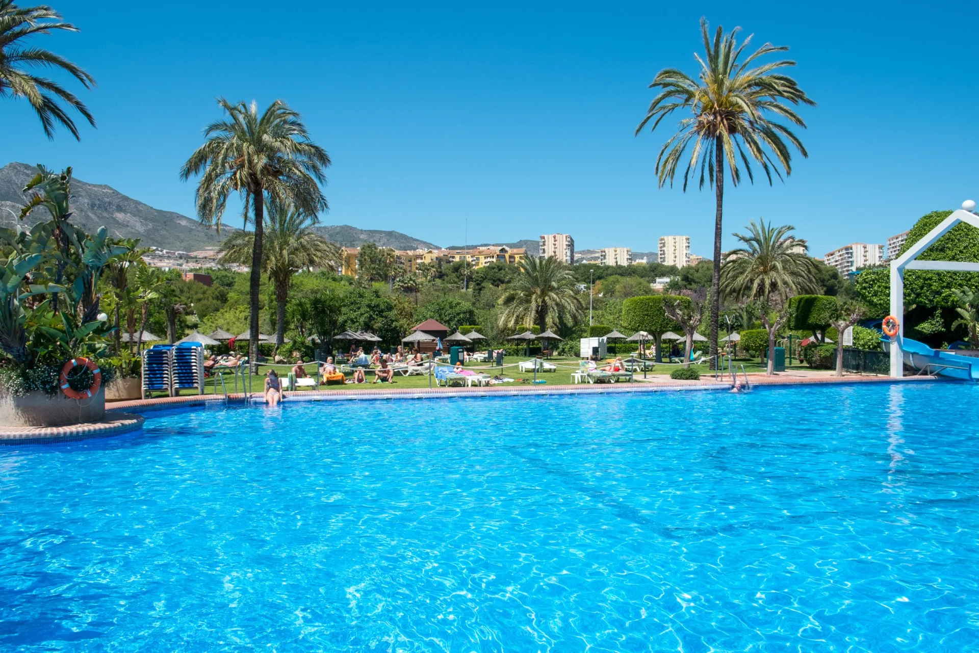 Large outdoor pool with palm trees, lawns and mountain views at Benal Beach