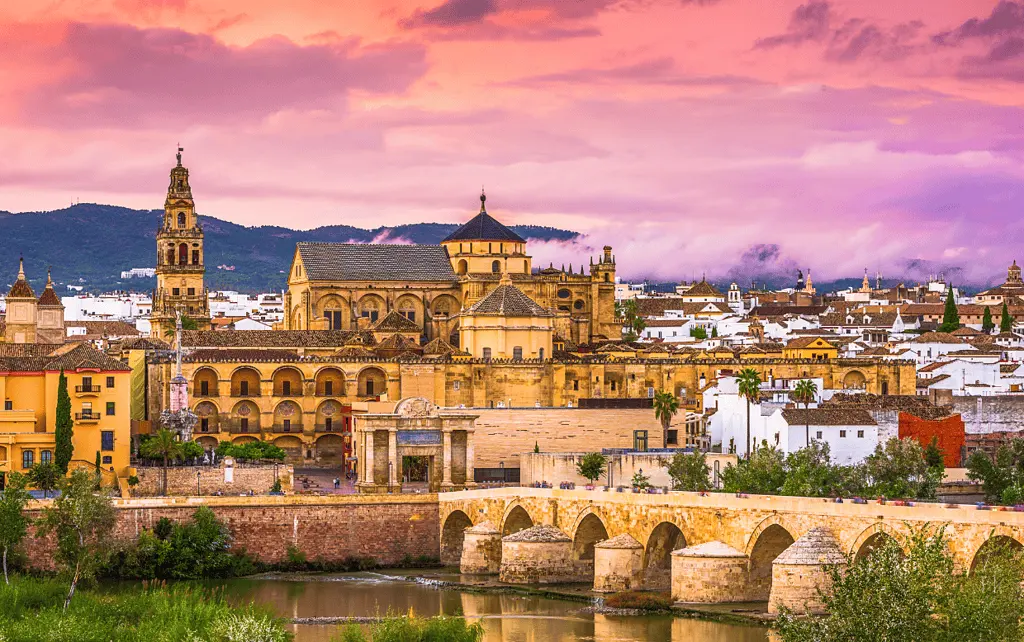 Roman Bridge and Mosque-Cathedral of Córdoba beneath a pink sunset sky