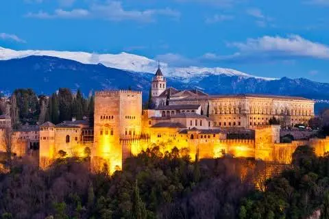 The illuminated Alhambra in Granada with the snow-capped Sierra Nevada mountains behind