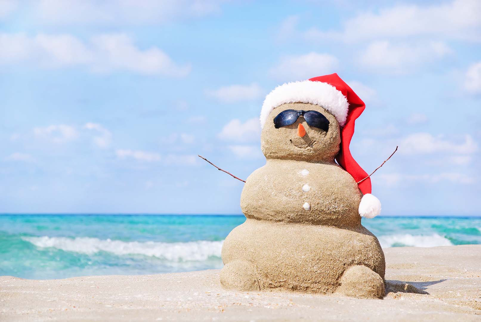 Benal Beach - Kingfisher Apartments - Un muñeco de nieve navideño con gorro de Papá Noel en una playa de arena - Alquileres de invierno a largo plazo